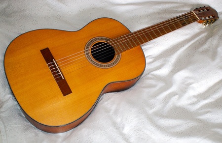 Classic wooden guitar on bed sheetの写真素材