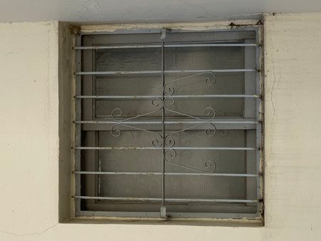 Old window with iron lattice on the wall of the house.