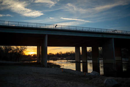 A silhouette of a bird on a bridge over a river at sunset
