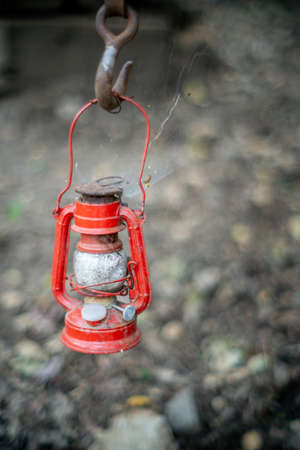 A red kerosene lamp hanging on a hook on the ground