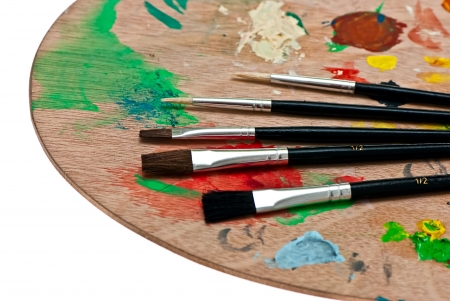 Wooden art palette with paint and brushes isolated on whiteの写真素材