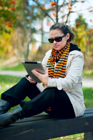 Young girl with tablet PC sitting on a park bench  Focus on the girl, the background is blurred の写真素材