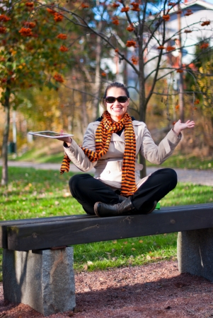 Young girl with tablet PC sitting on a park bench. Focus on the girl, the background is blurred.の写真素材