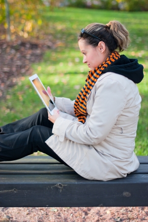 Young girl with tablet PC sitting on a park bench. Focus on the girl, the background is blurred.の写真素材