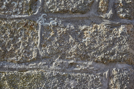 Very close shot of the texture of an ancient and traditional gray stone wall with brown tones, sunny light, very dark and sharp shadowsの写真素材