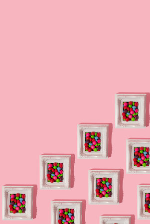Pattern made of a white picture frame full of multicoloured candies on pink background, above.