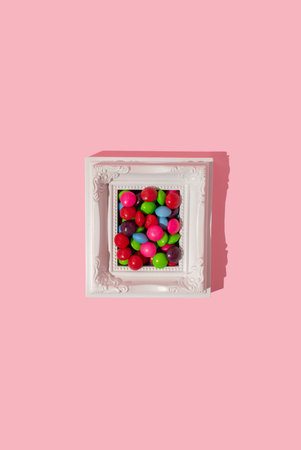White picture frame full of multicoloured candies on pink background, copy space