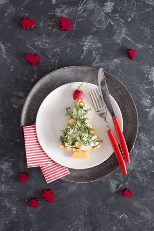 Savory tart with olives and dill, decorated like Christmas tree on white plate over gray table, minimal Christmas food decoration, flat layの写真素材