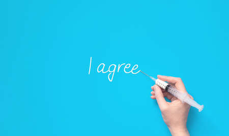 Hand holding syringe as a pen, signing agreement. Minimal vaccine concept.の写真素材