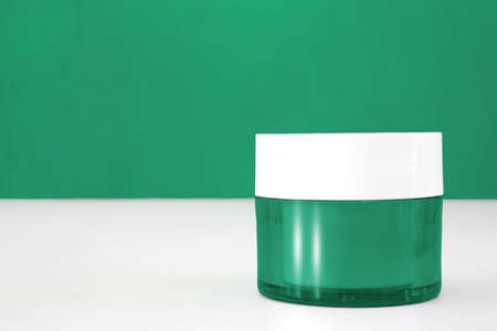 closed green plastic container for face cream on a green background and white table.の写真素材