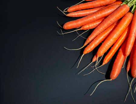 Healthy, juicy, fresh carrots in a strong contrast of orange and black background.の写真素材