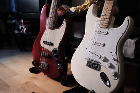 white electric guitar and red electric bass. both on a stand. Parquet floor.