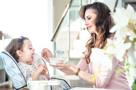 Pretty young mother feeding her beloved daughterの写真素材