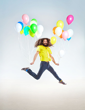 Conceptual portrait of a childish guy jumping with balloons