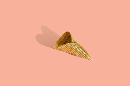 Golden ice cream cone with heart-shaped shadow on powder pink background. Minimal Conceptの写真素材