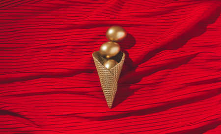 Golden Eggs in golden ice cream cone on the red textile background. Flat viewの写真素材