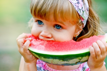 Adorable little girl eats a slice of watermelon outdoorsの写真素材