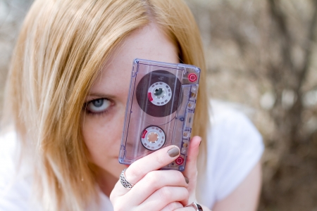 Beautiful girl with a cassette in hand near the fenceの写真素材