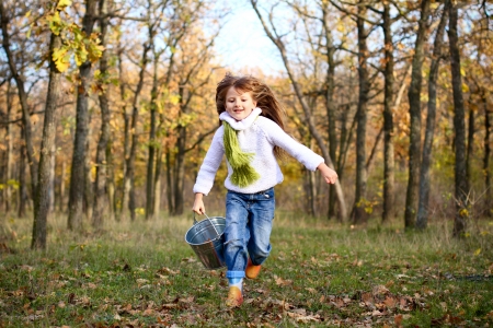 Little girl running with a bucket in the autumn forestの写真素材