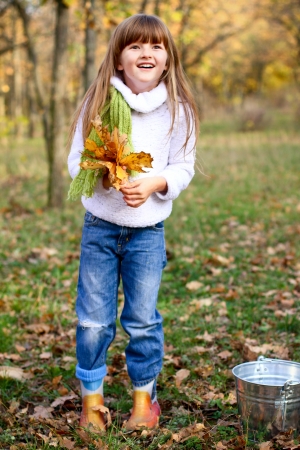 Little girl standing in the autumn forest with maple leaves and a bucketの写真素材