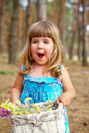 Enthusiastic little girl holding a basket of flowers in  forestの写真素材