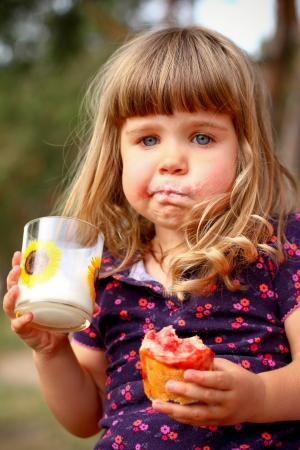 Little girl eating bread and drinks milk, outdoorsの写真素材