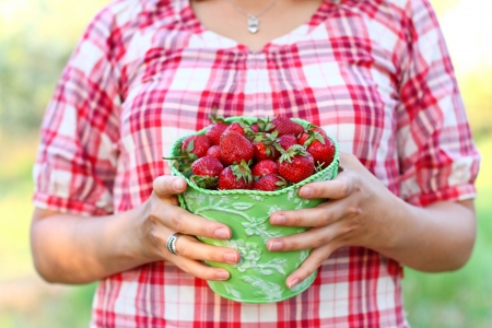 Young woman with  green pail of strawberries outdoorsの写真素材