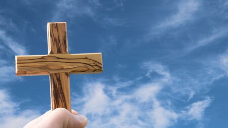 Hand holding christian cross into the blue sky