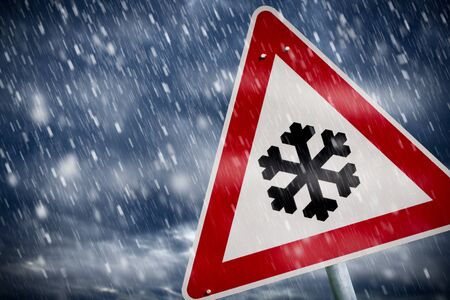 Snowfall on the road with a warning signの写真素材