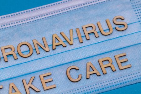 Wooden letters CORONAVIRUS TAKE CARE on protective medical mask.Coronavirus concept.