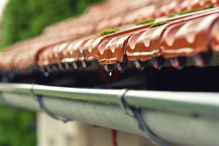 Drops of water flow into the eaves on the house in the rain.の写真素材