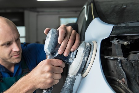 Grinder in the hands of a man who sharpen a car varnish in the car shop.の写真素材