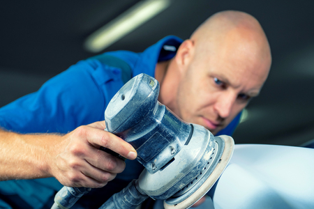 Grinder in the hands of a man who sharpen a car varnish in the car shop.の写真素材