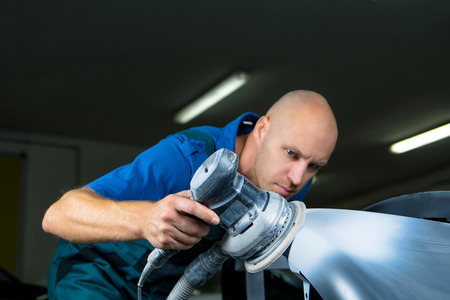 Grinder in the hands of a man who sharpen a car varnish in the car shop.の写真素材