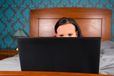 Woman lying on bed and looking at computer.の写真素材