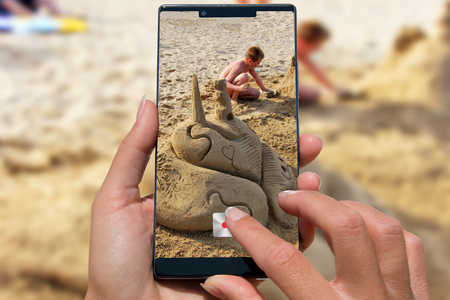 Woman with mobile phone photos boy with sand castle on the beach.の写真素材