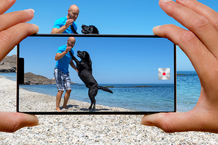 Woman with mobile phone photos man with his dog on the beach.の写真素材