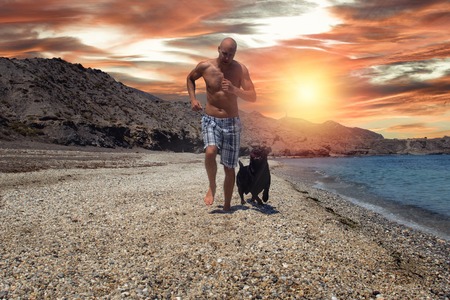 Man running with his dog on the beach at sunset.の写真素材