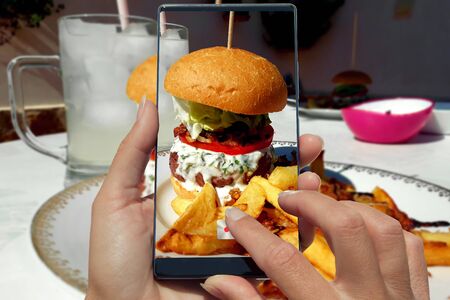 woman photographing on cell phone homemade hamburger and friesの写真素材