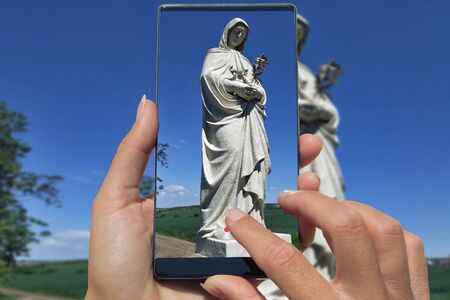 Woman photographing on cell phone statue of Mary praying in nature.の写真素材