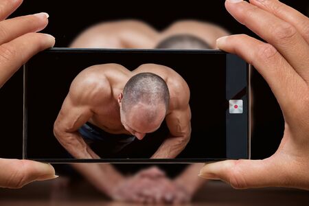 Woman photographing on cell phone muscular man doing push-ups. Fitness workout.の写真素材