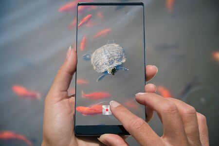 Woman photographing on cell phone water turtle and goldfish in river.の写真素材