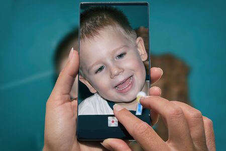 Woman photographing on cell phone cute young litle boy.の写真素材
