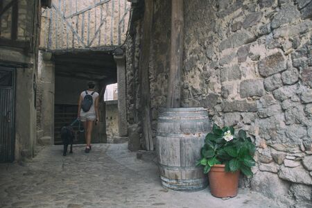 Woman with dog on vacation in streets of old mediterranean town with stone houses and flowers....