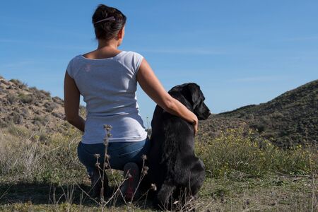 Labrador dog with woman sitting on ground and resting while walking in nature.