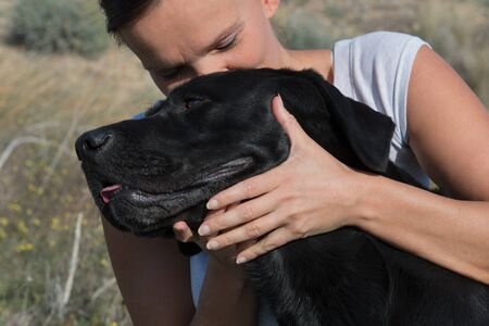 Woman sitting on ground cuddle and kiss Labrador dog while walking in nature.の写真素材