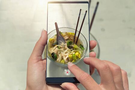 Woman photographing on cell phone homemade healthy food, Vietnamese soup pho.