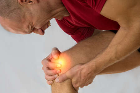 Health care concept man suffering from knee pain on light background.の写真素材