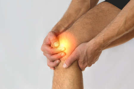 Health care concept man suffering from knee pain on light background.の写真素材