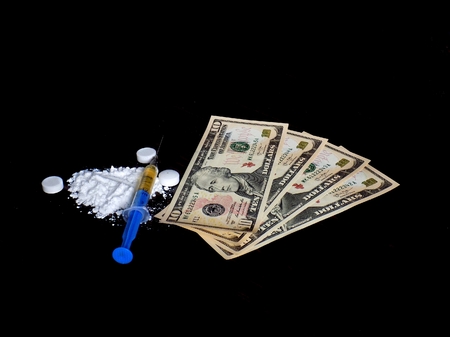 Injection syringe on cocaine drug powder, pills and dollar money bills on black background